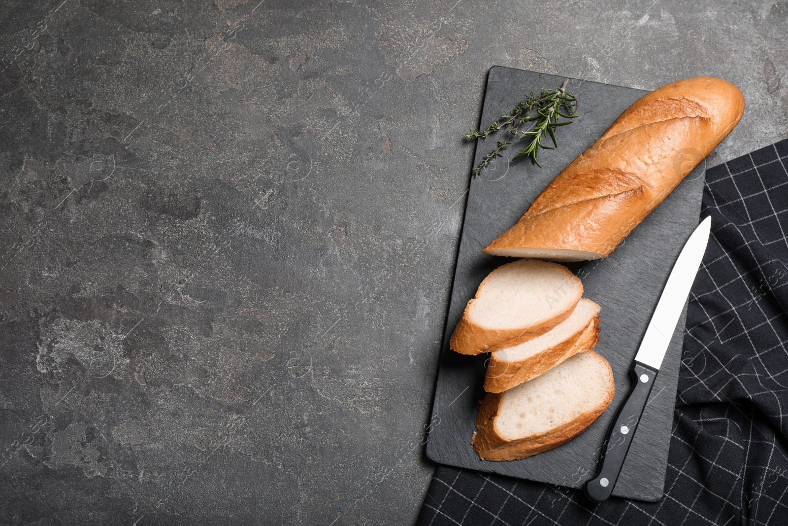 Photo of Cut tasty baguette with knife on grey table, flat lay. Space for text