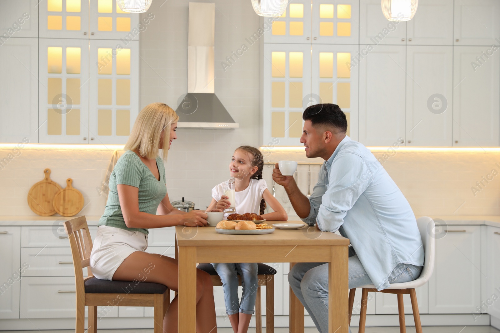 Photo of Happy family eating together at table in modern kitchen