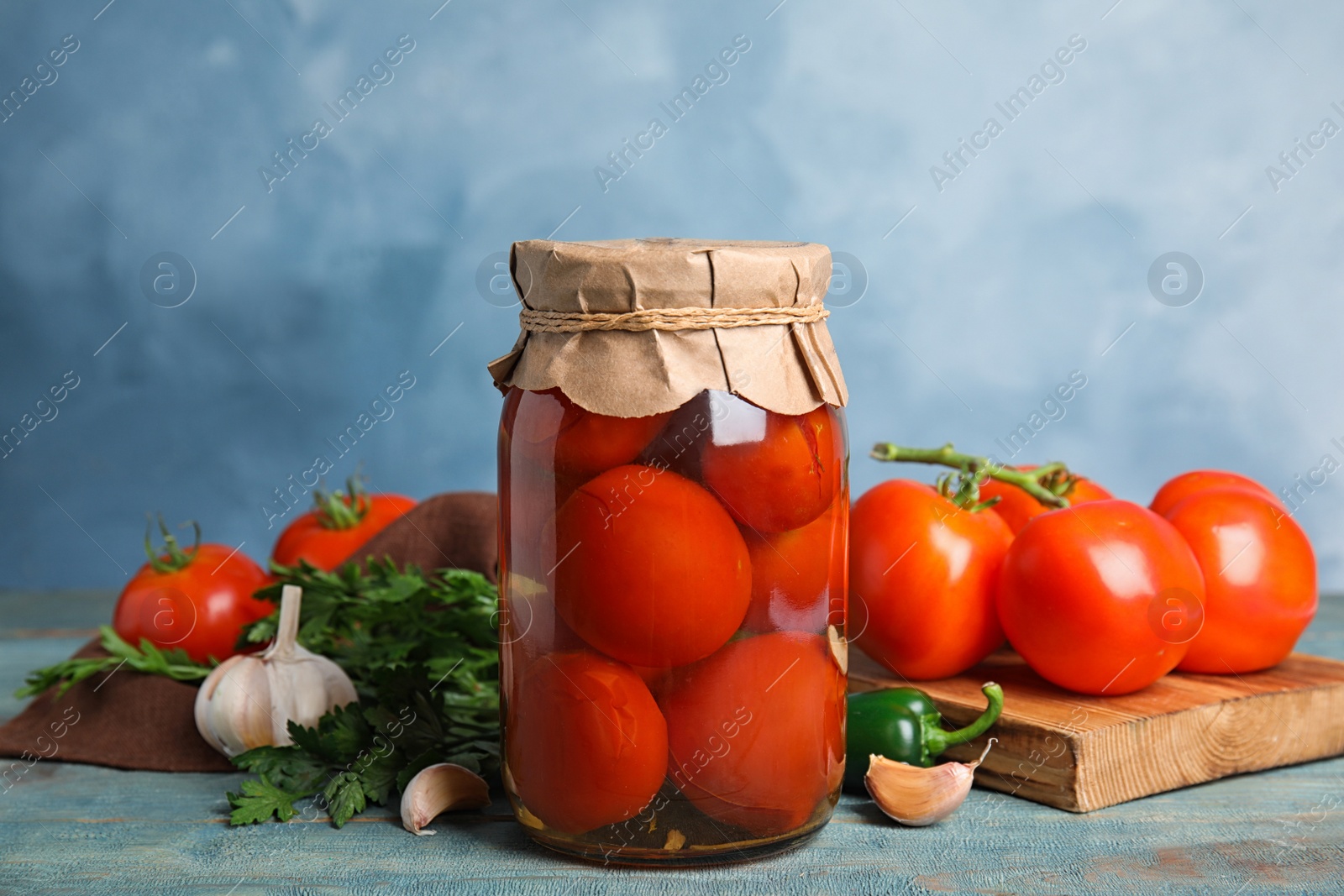 Photo of Pickled tomatoes in glass jar and products on wooden table against blue background