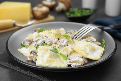 Photo of Delicious ravioli with tasty sauce and mushrooms served on black table, closeup