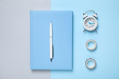 Light blue notebook, alarm clock and tapes on color background, flat lay