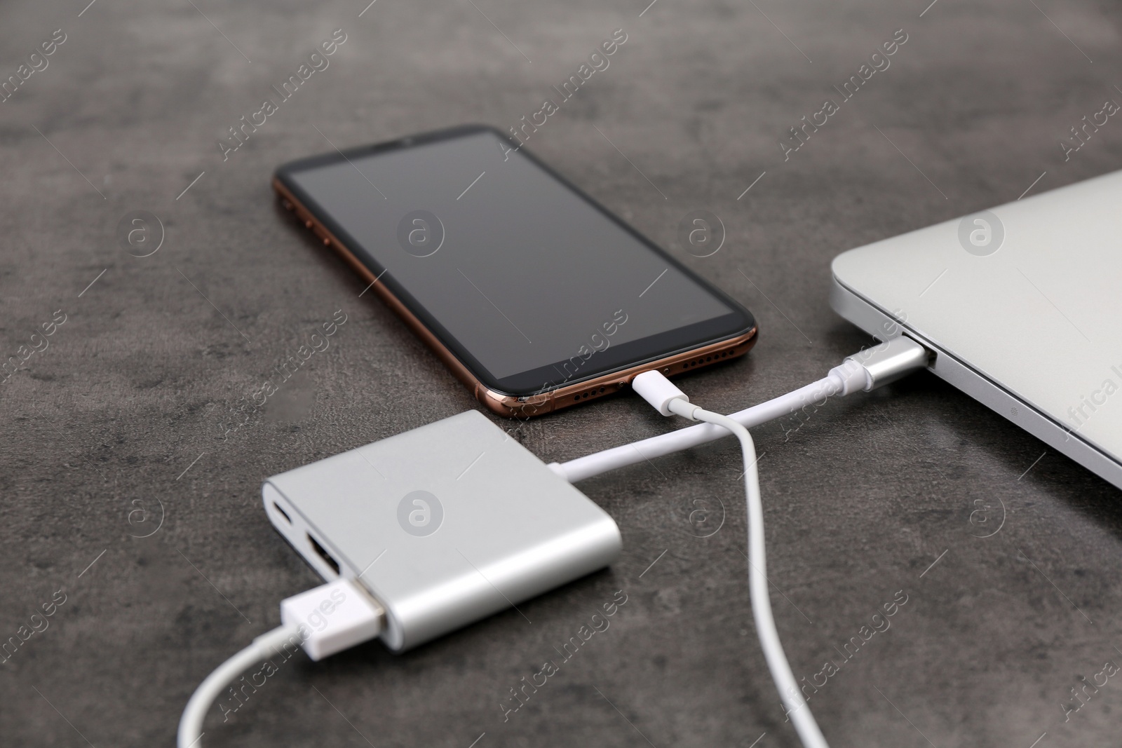 Photo of Modern smartphone and laptop charging from power bank on grey table, closeup