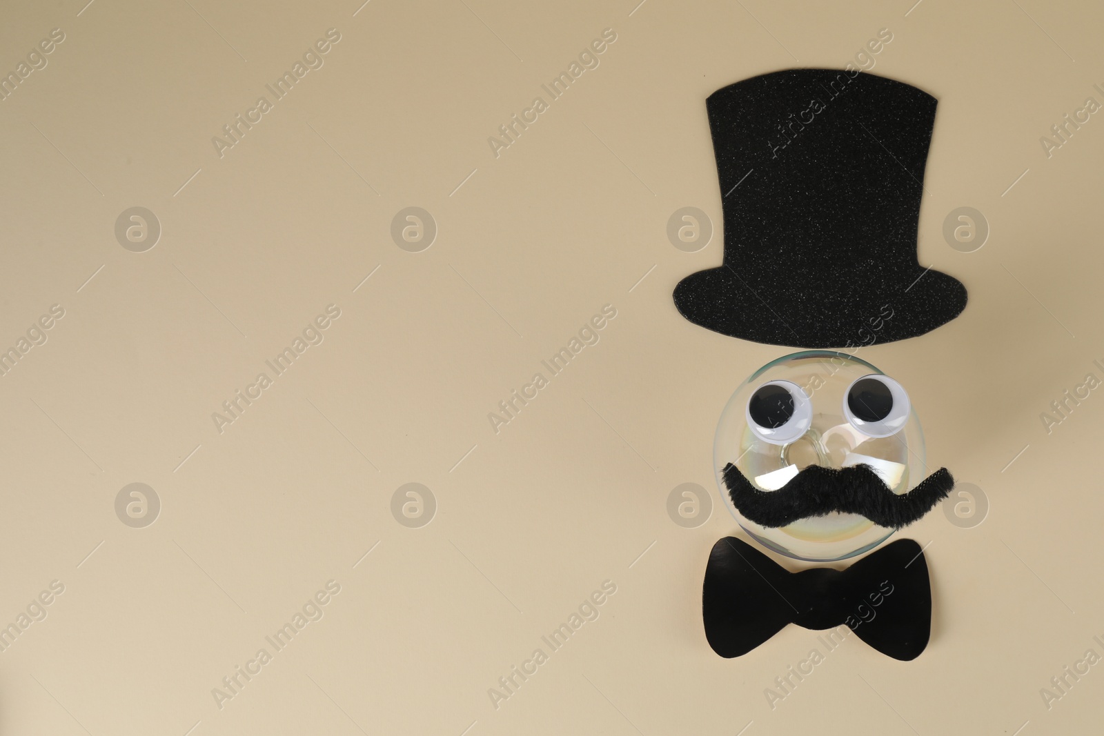 Photo of Man's face made of fake mustache, ball, hat, bow tie and eyes on beige background, top view. Space for text
