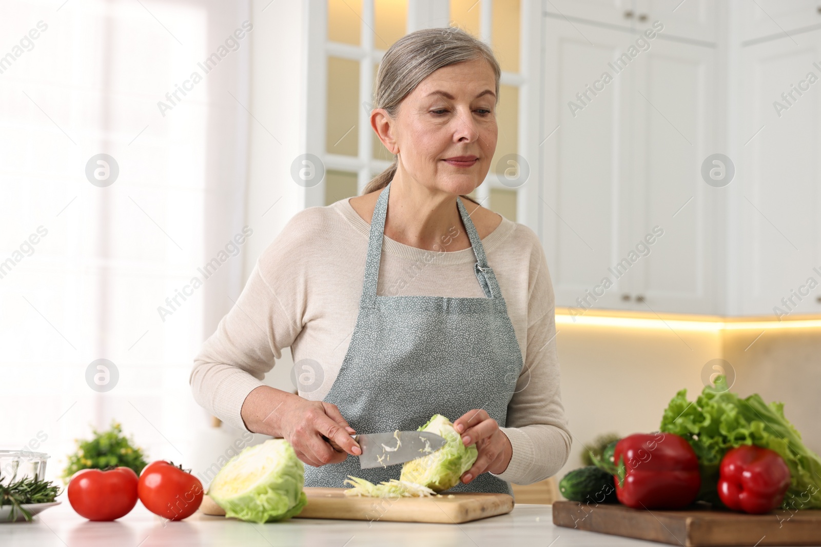 Photo of Happy housewife cutting cabbage at table in kitchen