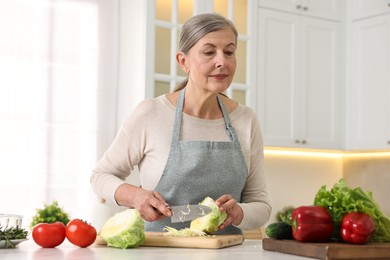 Happy housewife cutting cabbage at table in kitchen