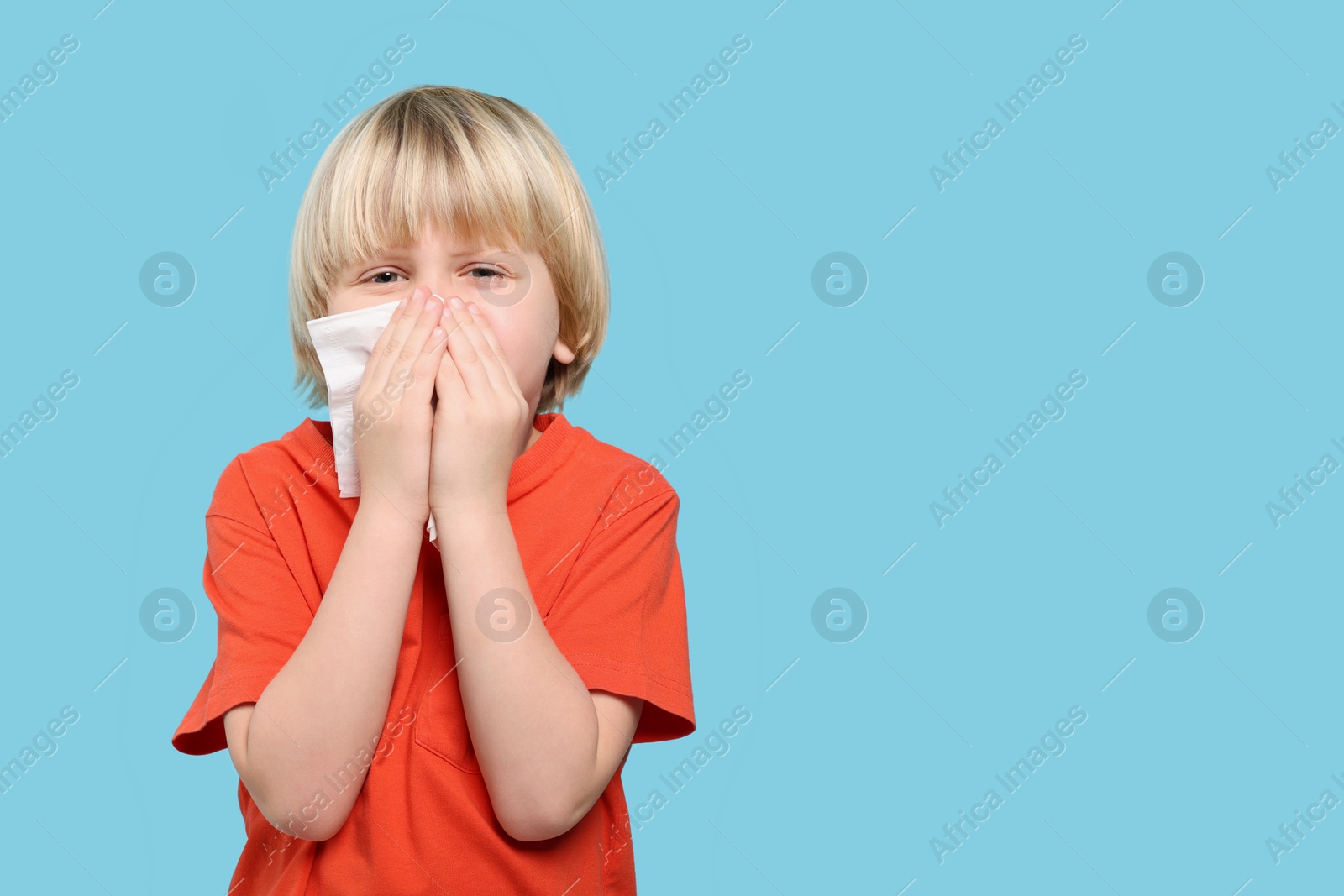 Photo of Boy blowing nose in tissue on light blue background, space for text. Cold symptoms