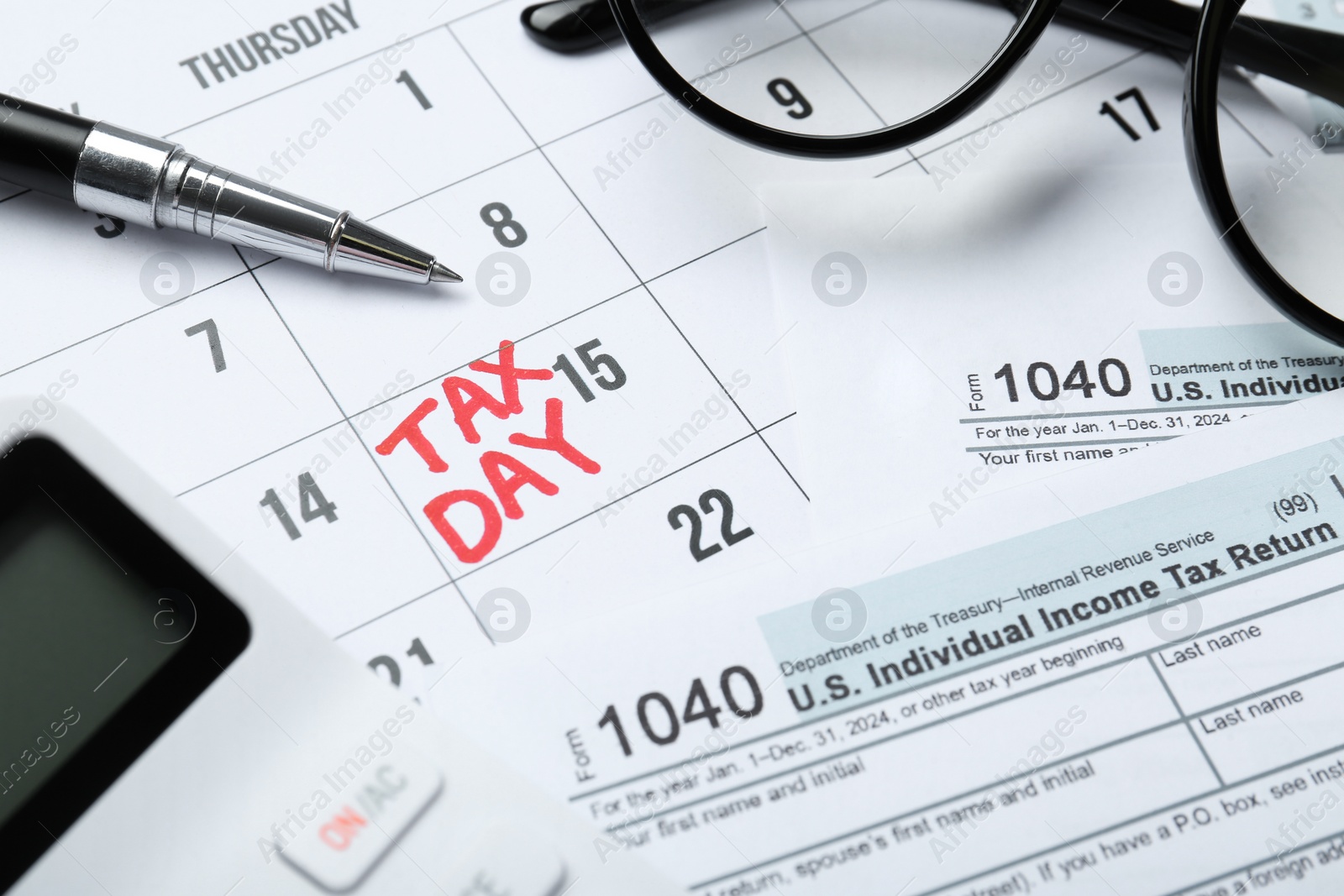 Photo of Calendar with date reminder about tax day, documents, glasses, pen and calculator, closeup