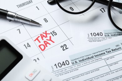 Photo of Calendar with date reminder about tax day, documents, glasses, pen and calculator, closeup