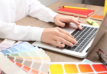 Photo of Woman working with laptop and palette samples at wooden table, closeup