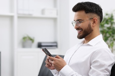 Happy young man using smartphone in office, space for text