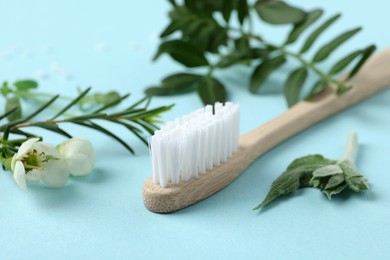 Photo of Bamboo toothbrush, beautiful flowers and herbs on light blue background, closeup