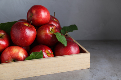 Photo of Juicy red apples in wooden tray on grey table
