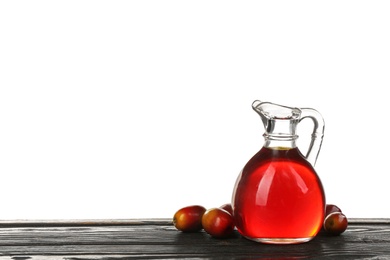 Palm oil in glass jug and fruits on black wooden table against white background