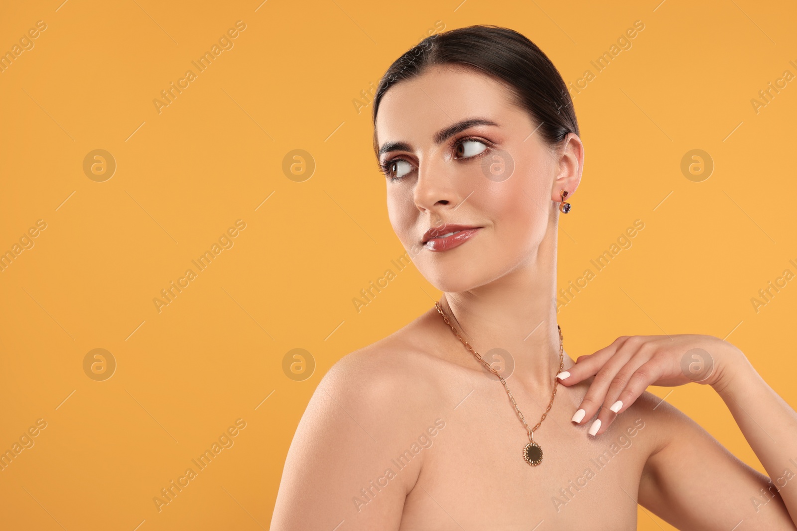 Photo of Beautiful woman with elegant jewelry on orange background, space for text