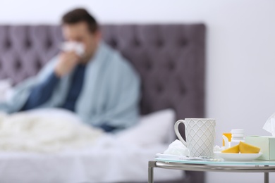 Photo of Table with cold remedies and blurred sick man on background