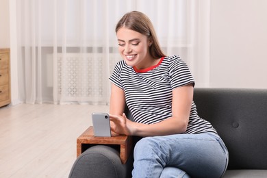 Photo of Happy woman using smartphone on sofa armrest wooden table at home, space for text