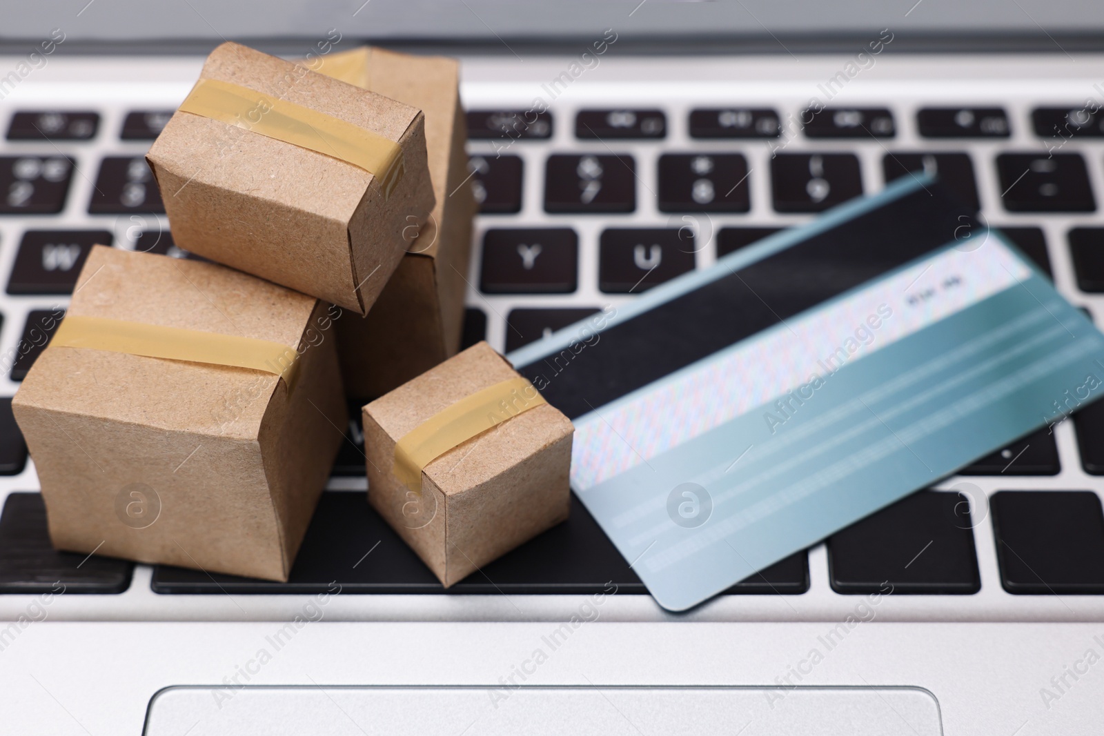 Photo of Internet shopping. Small cardboard boxes and credit card on laptop, closeup