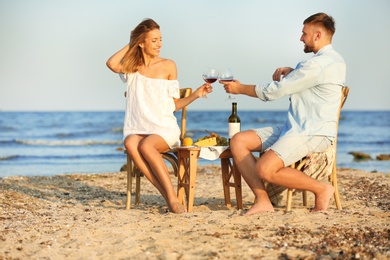 Photo of Young couple with glasses of wine having romantic dinner on beach