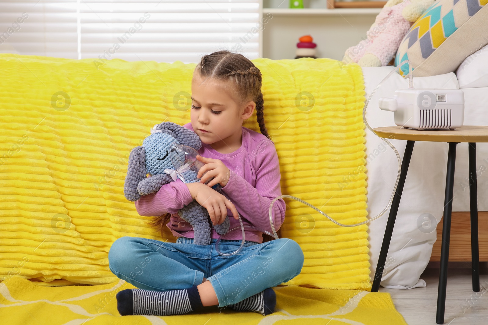 Photo of Little girl with toy bunny and nebulizer for inhalation on floor at home