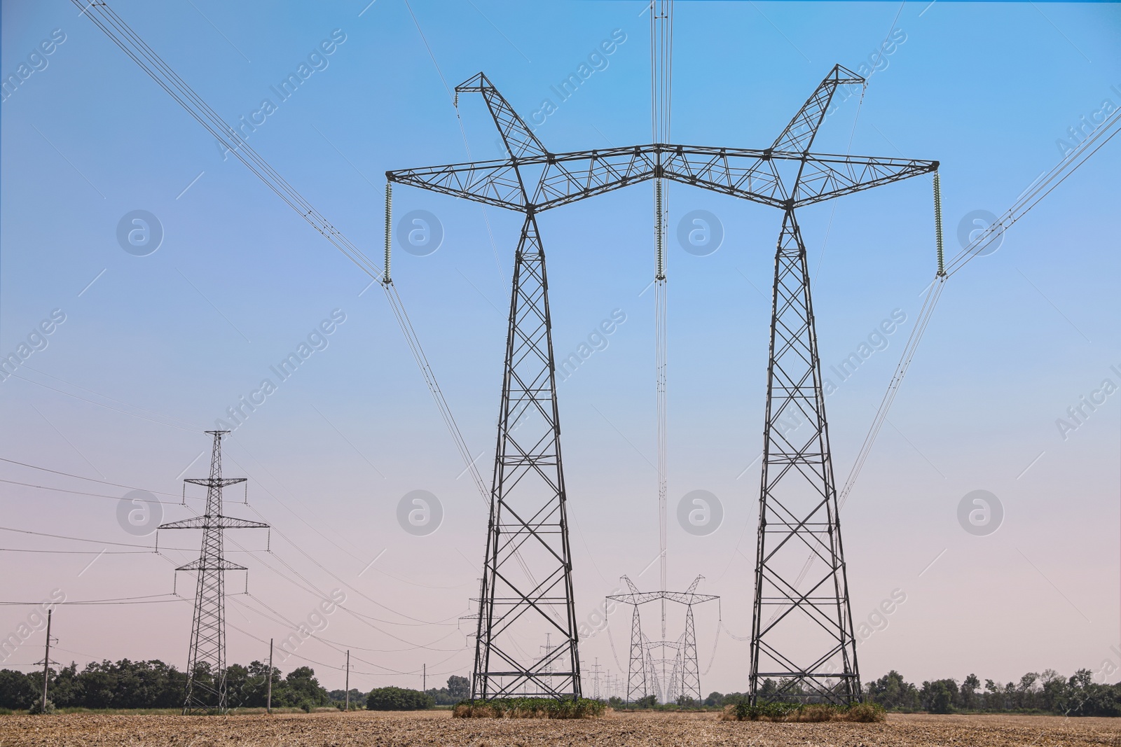 Photo of High voltage towers with electricity transmission power lines in field on sunny day