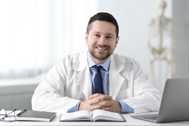 Photo of Smiling doctor with laptop at table in clinic. Online medicine
