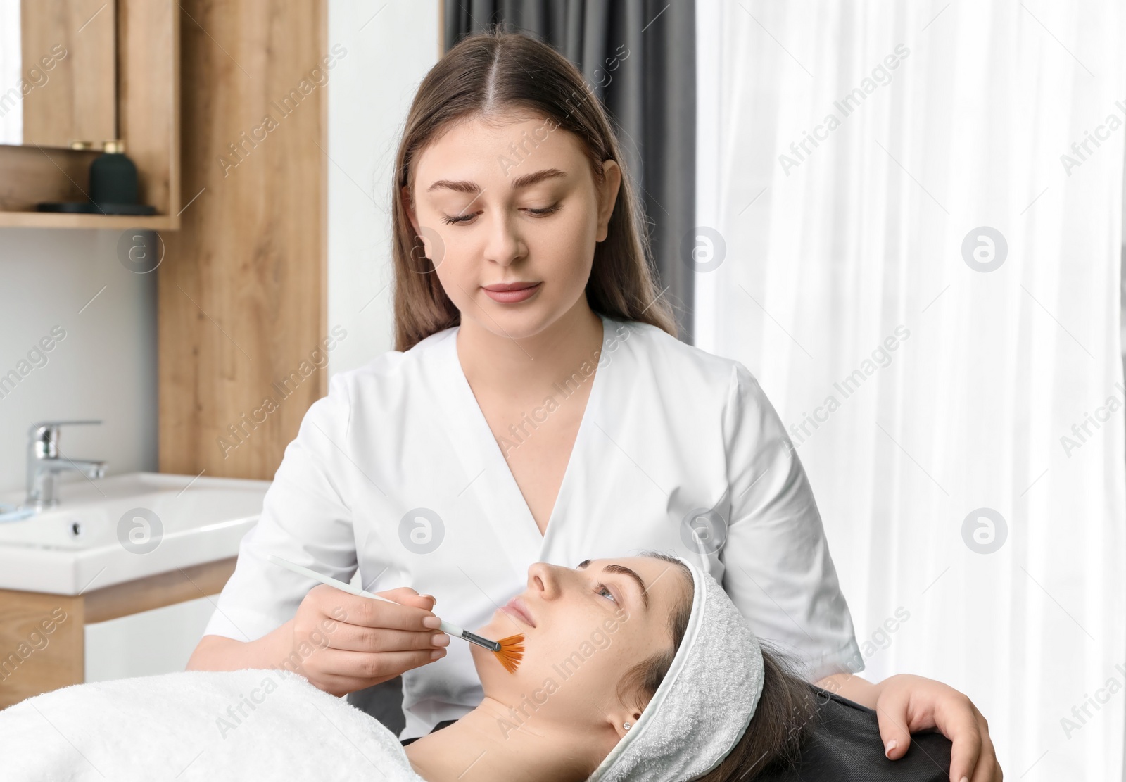 Photo of Cosmetologist with brush applying cosmetic product to client`s face in clinic