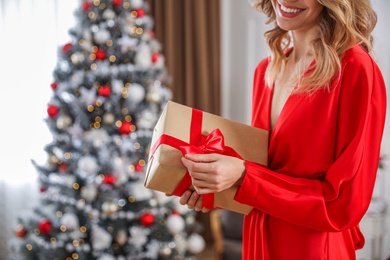 Photo of Young woman with present near Christmas tree at home, closeup