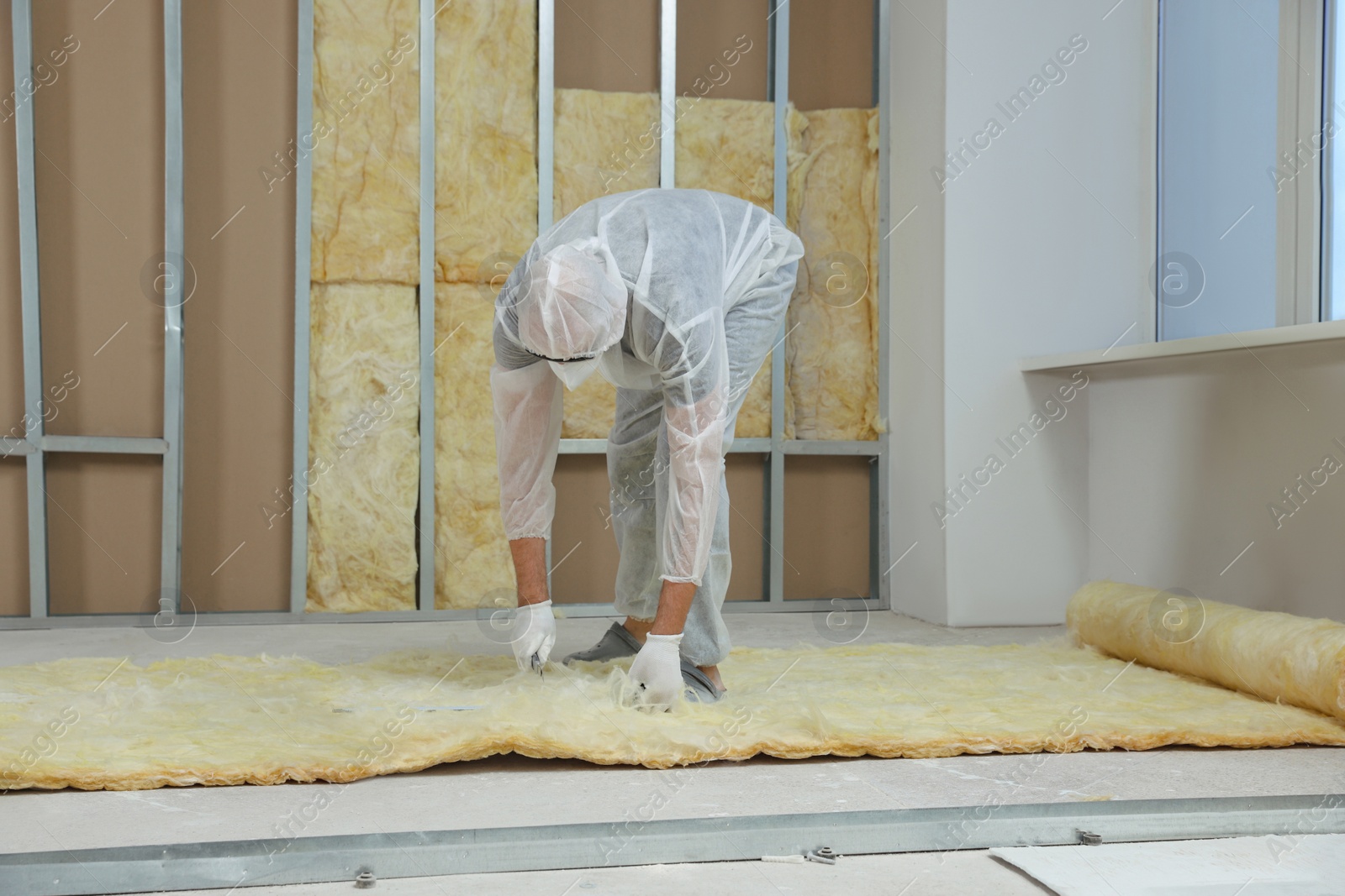 Photo of Worker measuring and cutting insulation material indoors