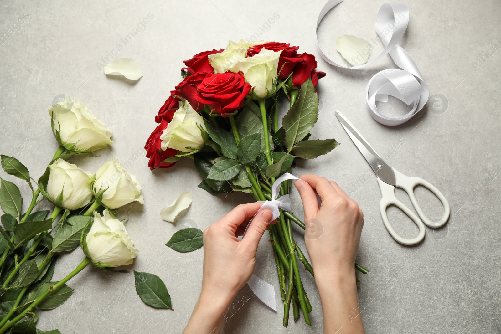 Photo of Woman making luxury bouquet of fresh roses at grey table, top view