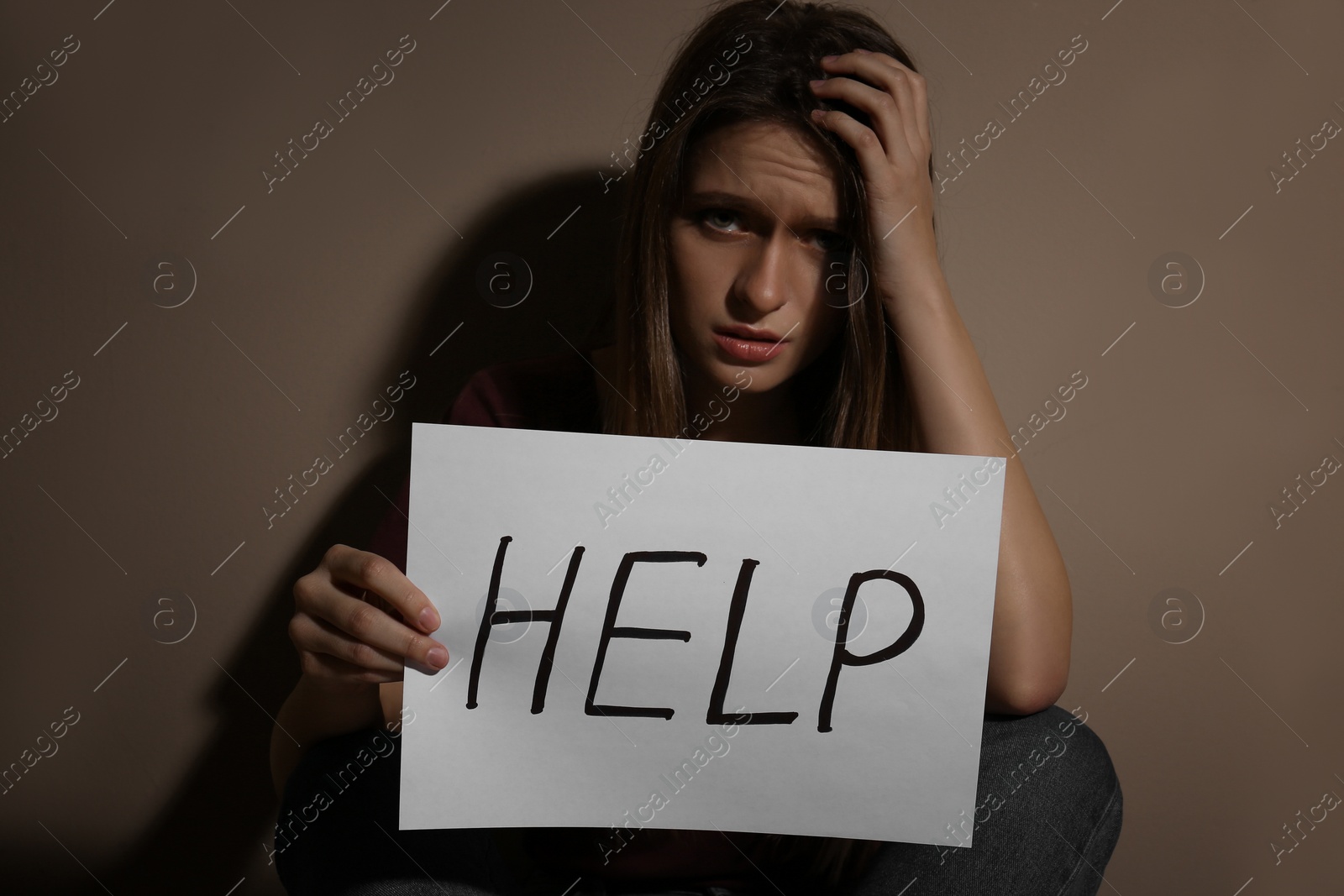 Photo of Abused young woman with sign HELP near beige wall. Domestic violence concept