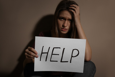 Photo of Abused young woman with sign HELP near beige wall. Domestic violence concept