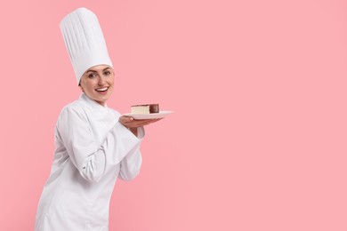 Photo of Happy professional confectioner in uniform holding delicious cheesecake on pink background. Space for text