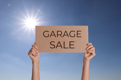 Woman holding sign with text GARAGE SALE against blue sky