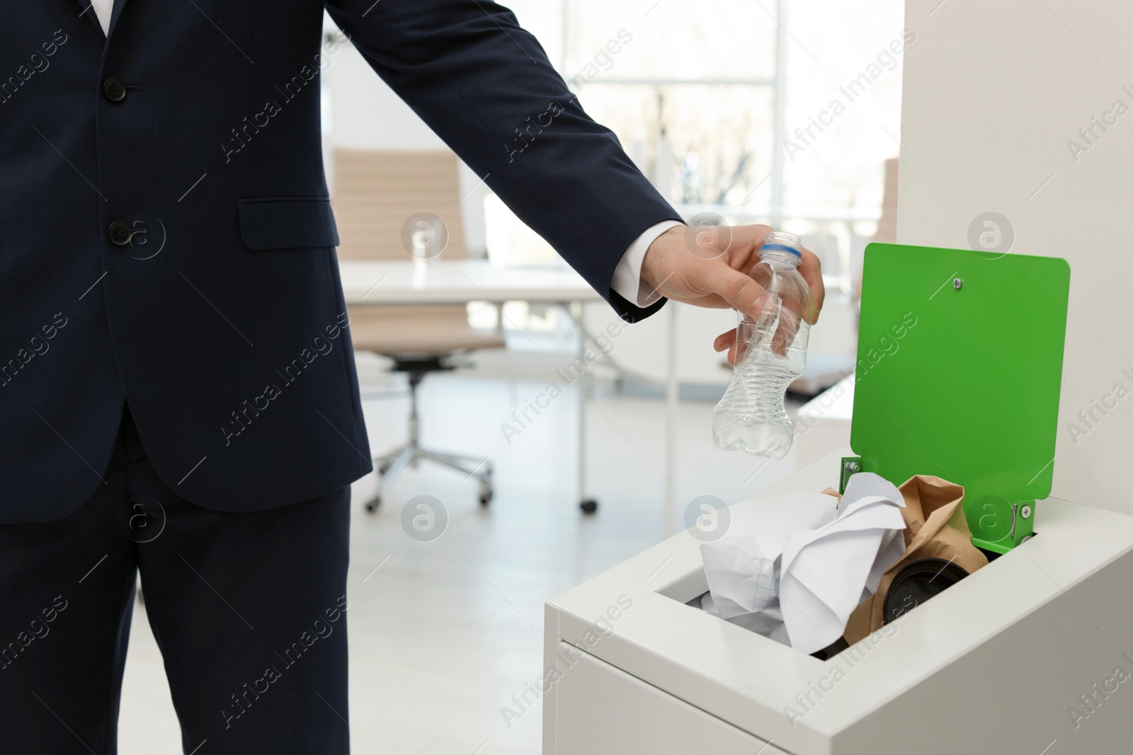 Photo of Man putting used plastic bottle into trash bin in office, closeup. Waste recycling