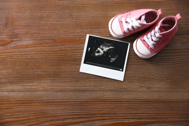 Photo of Ultrasound picture and baby shoes on wooden background, top view with space for text