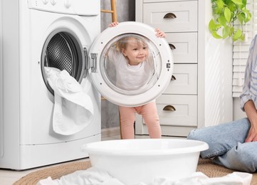 Happy mother with her daughter washing baby clothes in bathroom