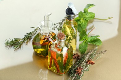 Photo of Cooking oil with different spices and herbs in bottles on beige table, above view