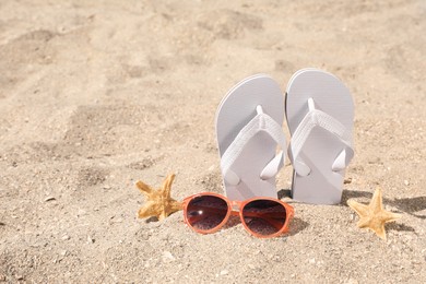 Photo of Stylish flip flops, sunglasses and starfishes on sand, space for text