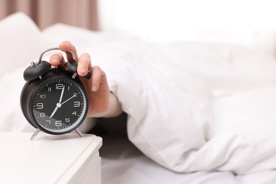 Man turning off alarm clock in bedroom, focus on hand. Space for text