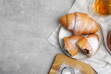 Flat lay composition with tasty croissants, tea and sugar powder on light grey table. Space for text