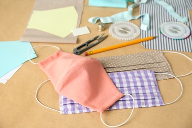 Photo of Fabric, sewing accessories and cloth masks on brown background. Personal protective equipment during COVID-19 pandemic