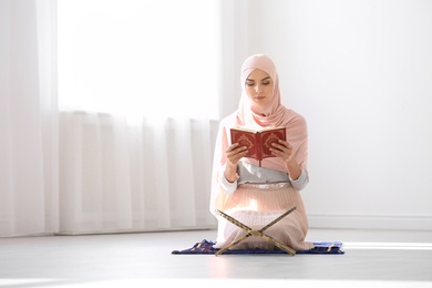 Muslim woman in hijab reading Koran indoors