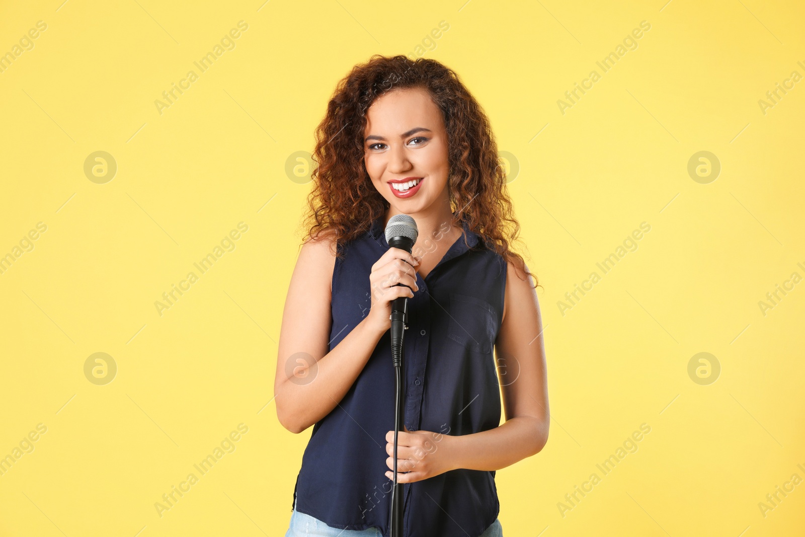 Photo of Portrait of curly African-American woman posing with microphone on color background