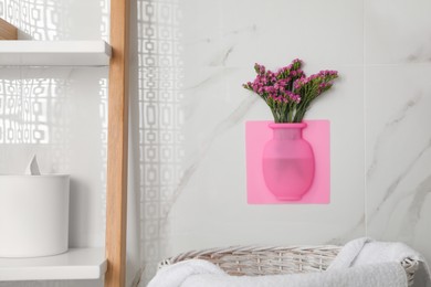 Photo of Silicone vase with flowers on white marble wall in bathroom