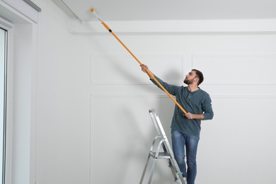 Photo of Young man painting ceiling with white dye indoors