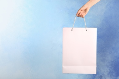 Woman holding paper shopping bag on color background