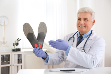 Photo of Senior male orthopedist showing insoles in clinic
