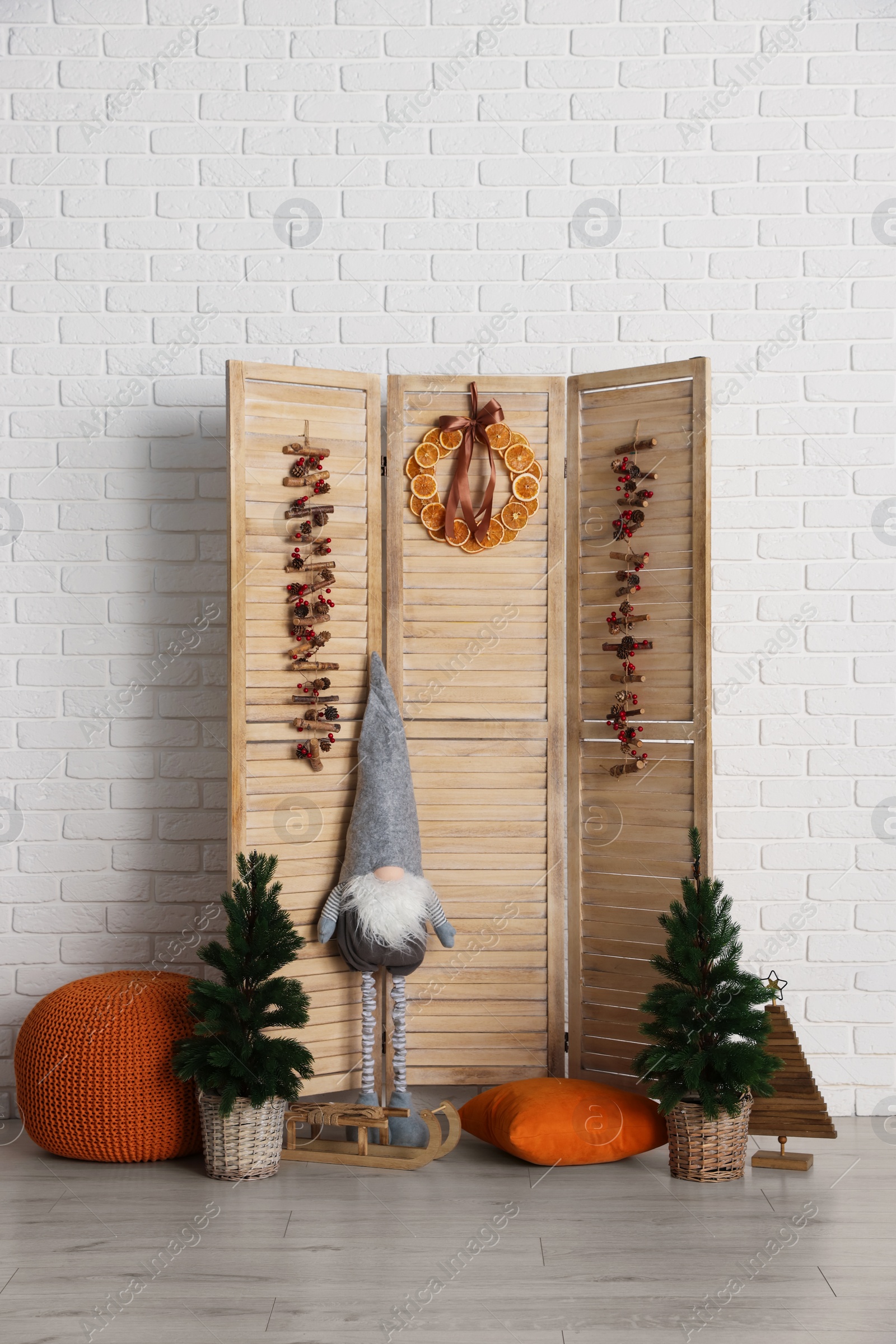 Photo of Beautiful Christmas themed photo zone with small trees, dwarf and fir decor near white brick wall