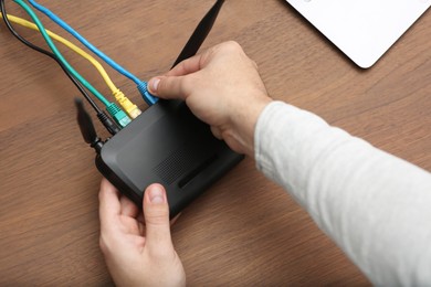 Man inserting cable into Wi-Fi router at wooden table, closeup