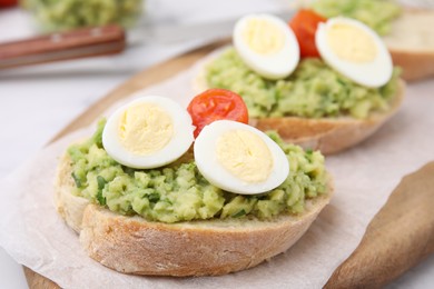 Delicious sandwiches with guacamole, eggs and tomatoes on parchment paper, closeup